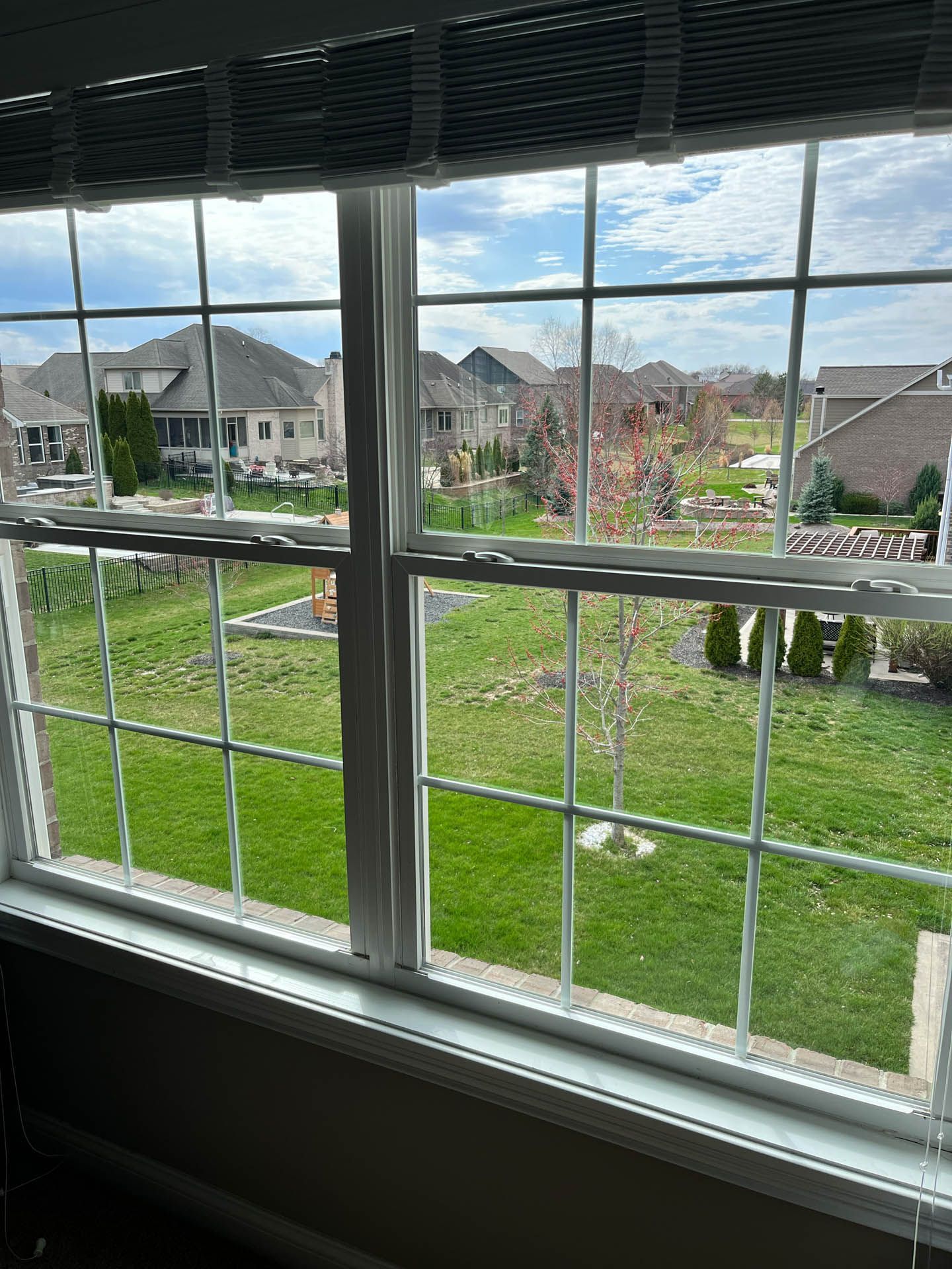 View through a window of a grassy suburban neighborhood under a partly cloudy sky.