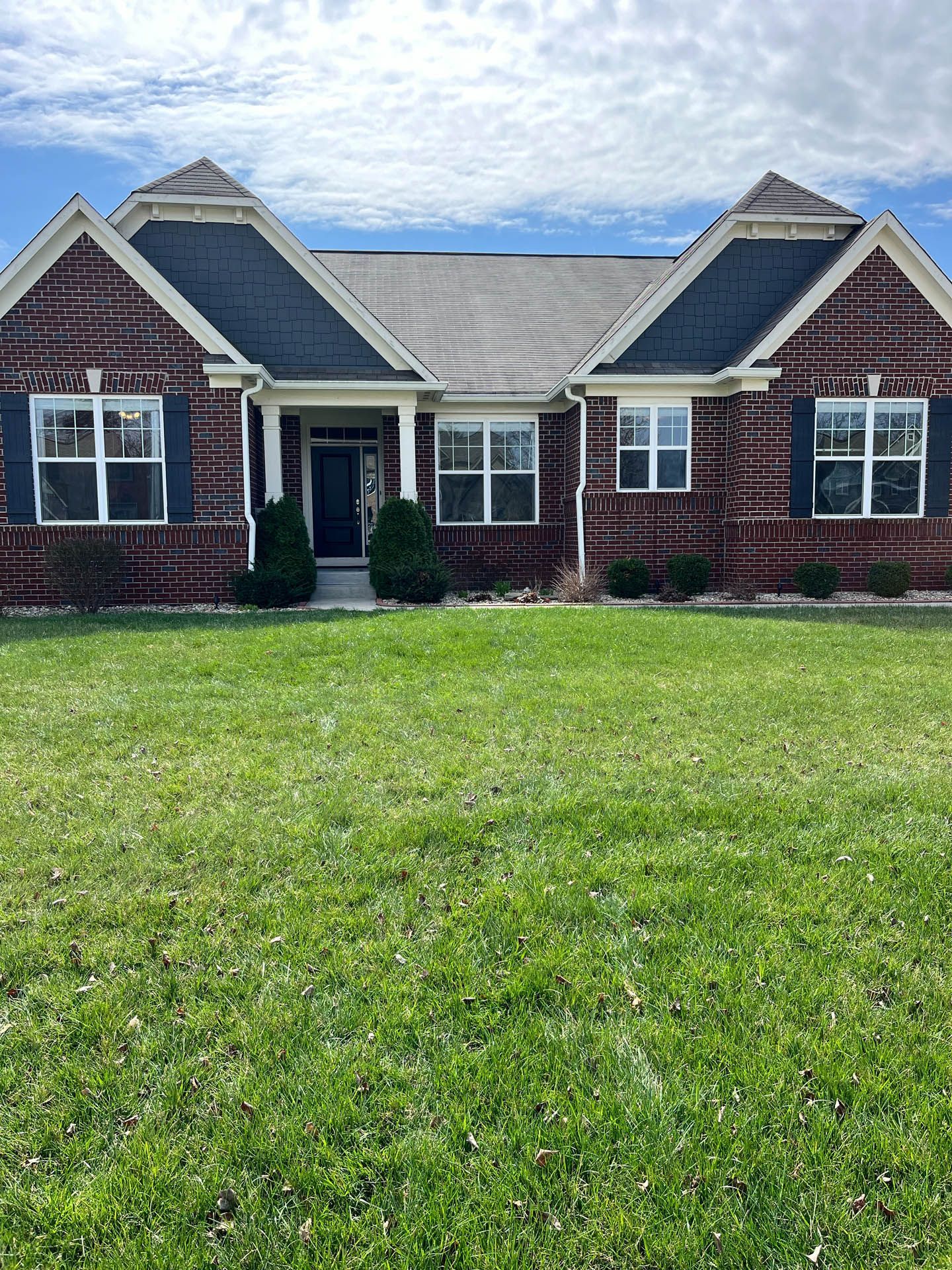 Brick house with white trim, blue roof, and a green lawn under a partly cloudy sky