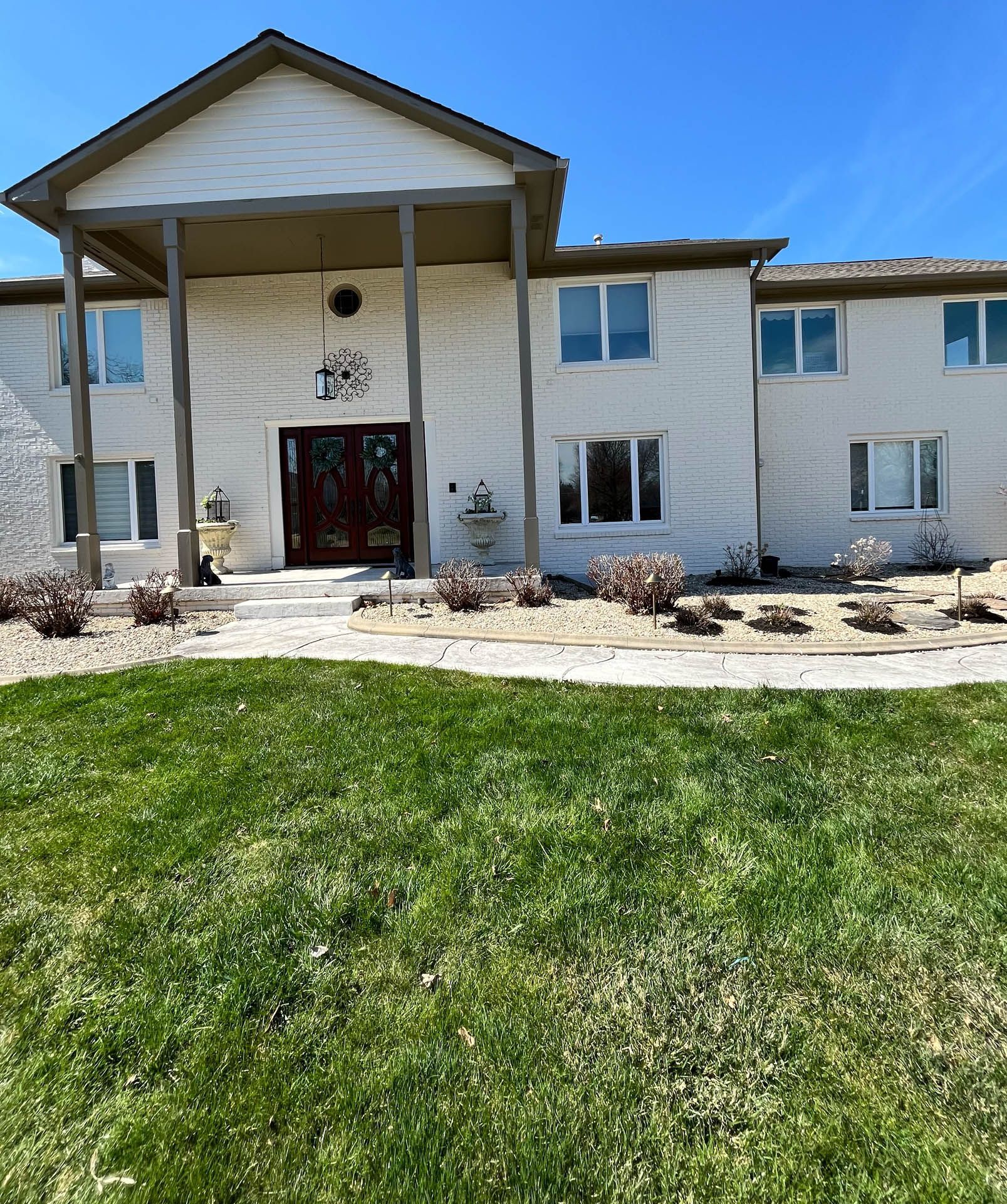 White two-story house with a covered front entrance, dark doors, and a green lawn under a blue sky