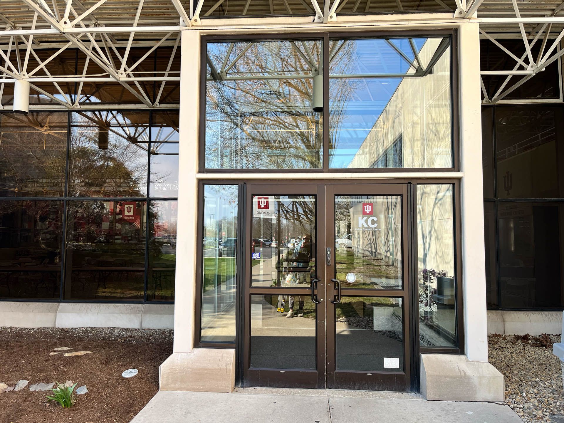 Glass double doors at a building entrance beneath a metal awning, with reflective windows and a concrete walkway