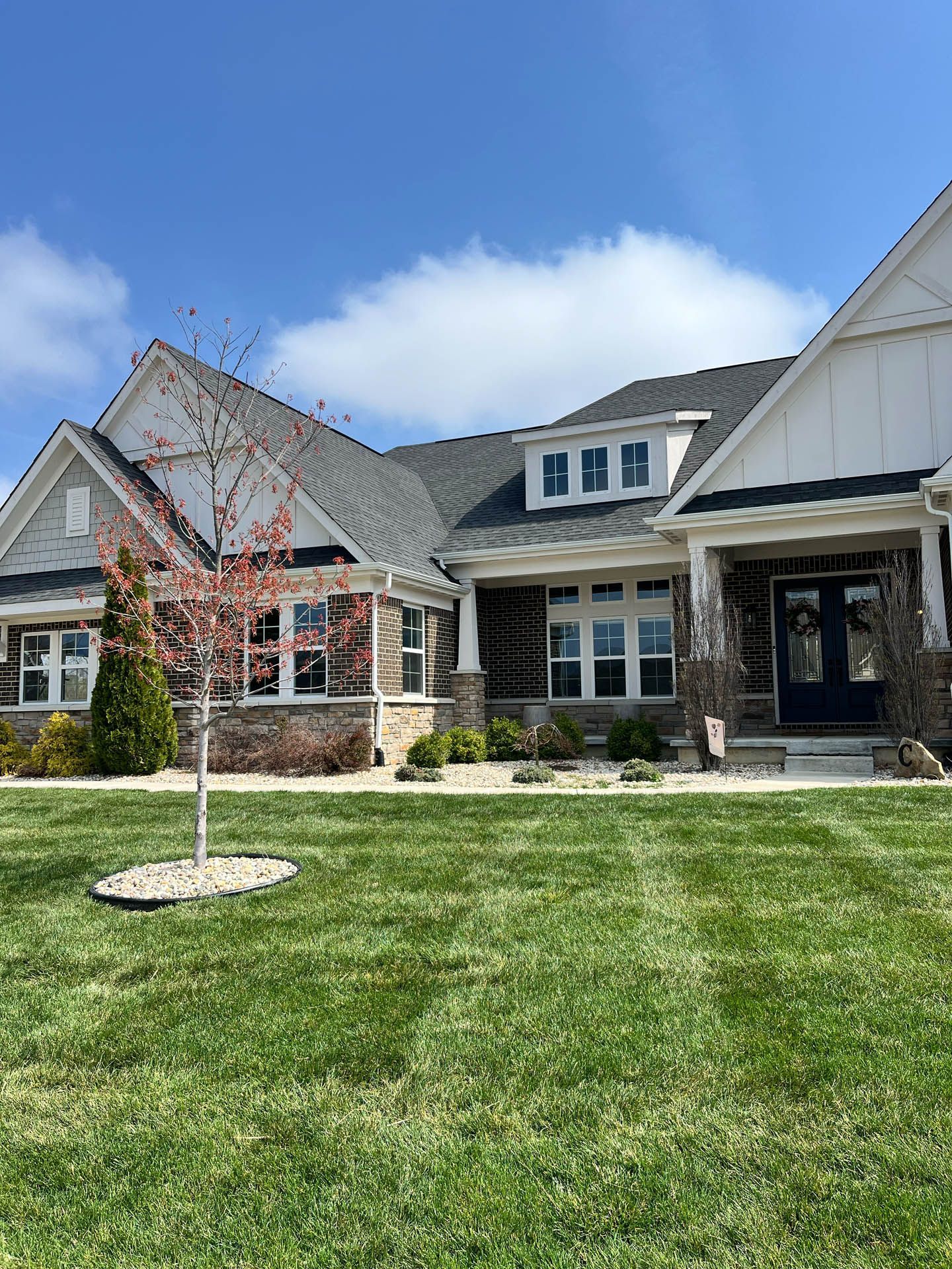 Suburban house with stone and white siding, front lawn, small tree, and blue sky.