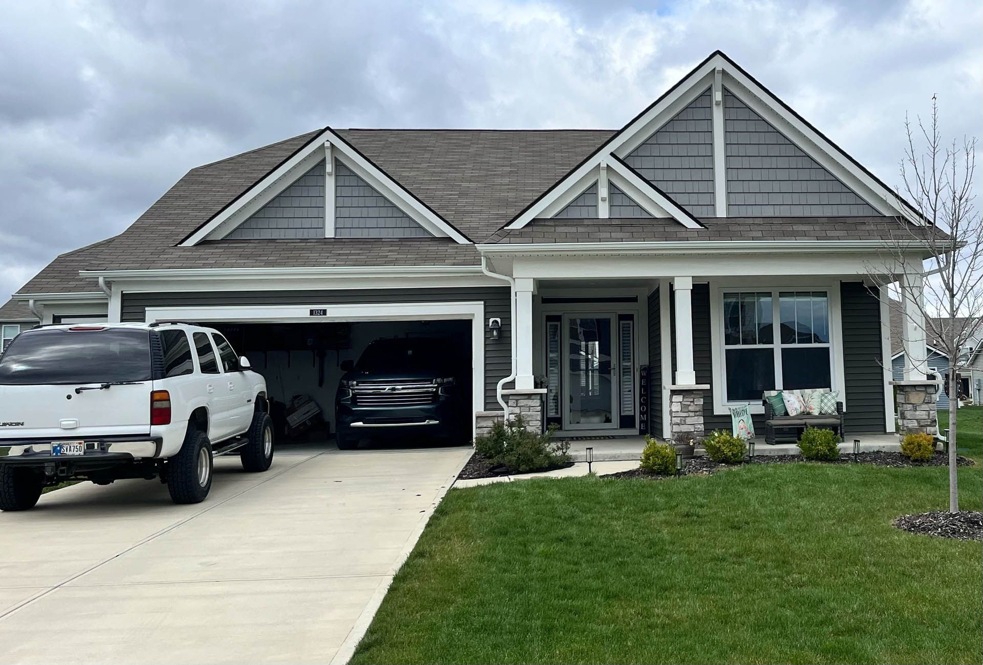 Suburban house with open garage, white pickup truck, and manicured lawn under a cloudy sky