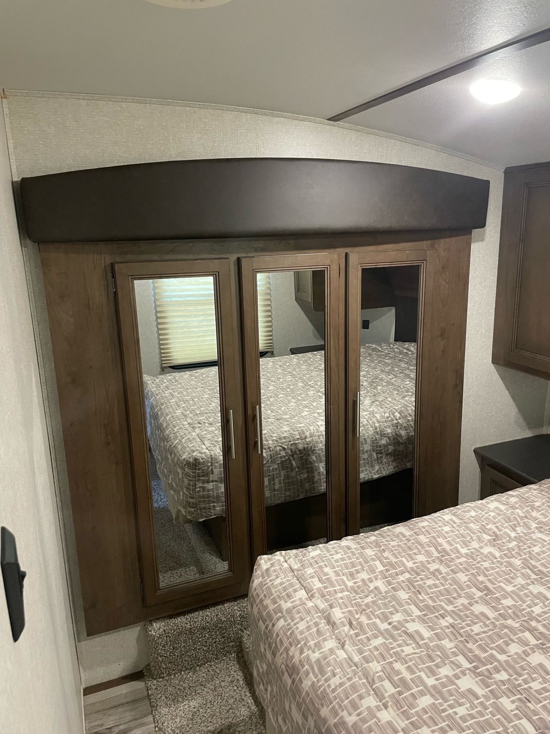 A bedroom with a bed , mirrored doors , and a window.