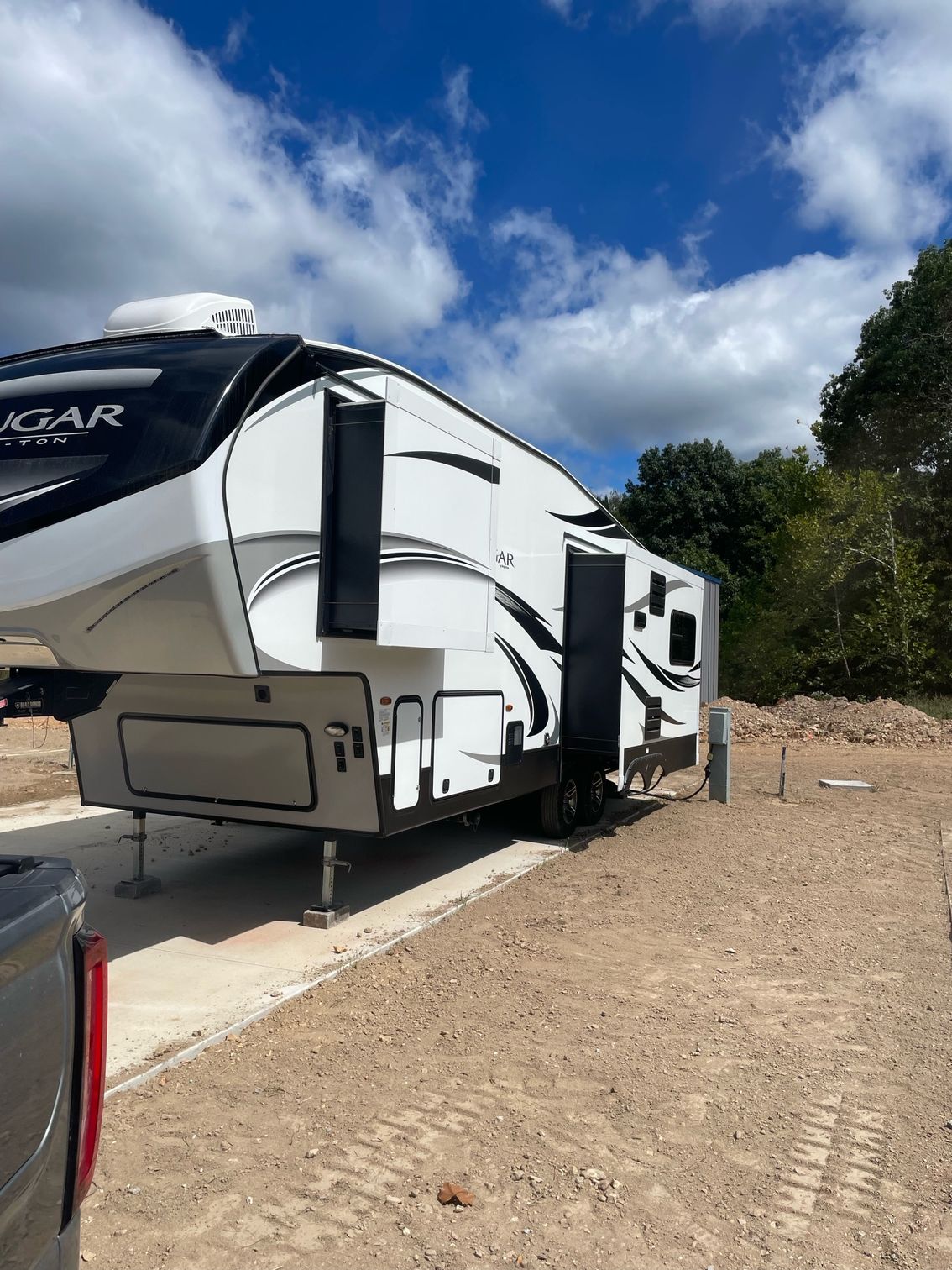 A white rv is parked in a dirt lot next to a truck.
