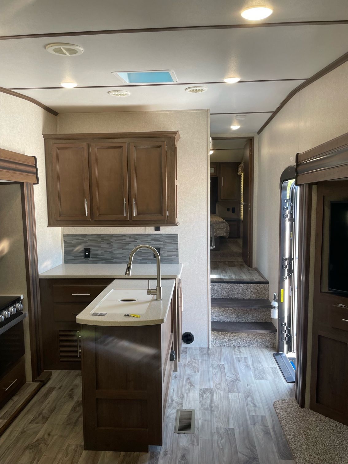 A kitchen in a trailer with a sink , stove , cabinets and stairs.