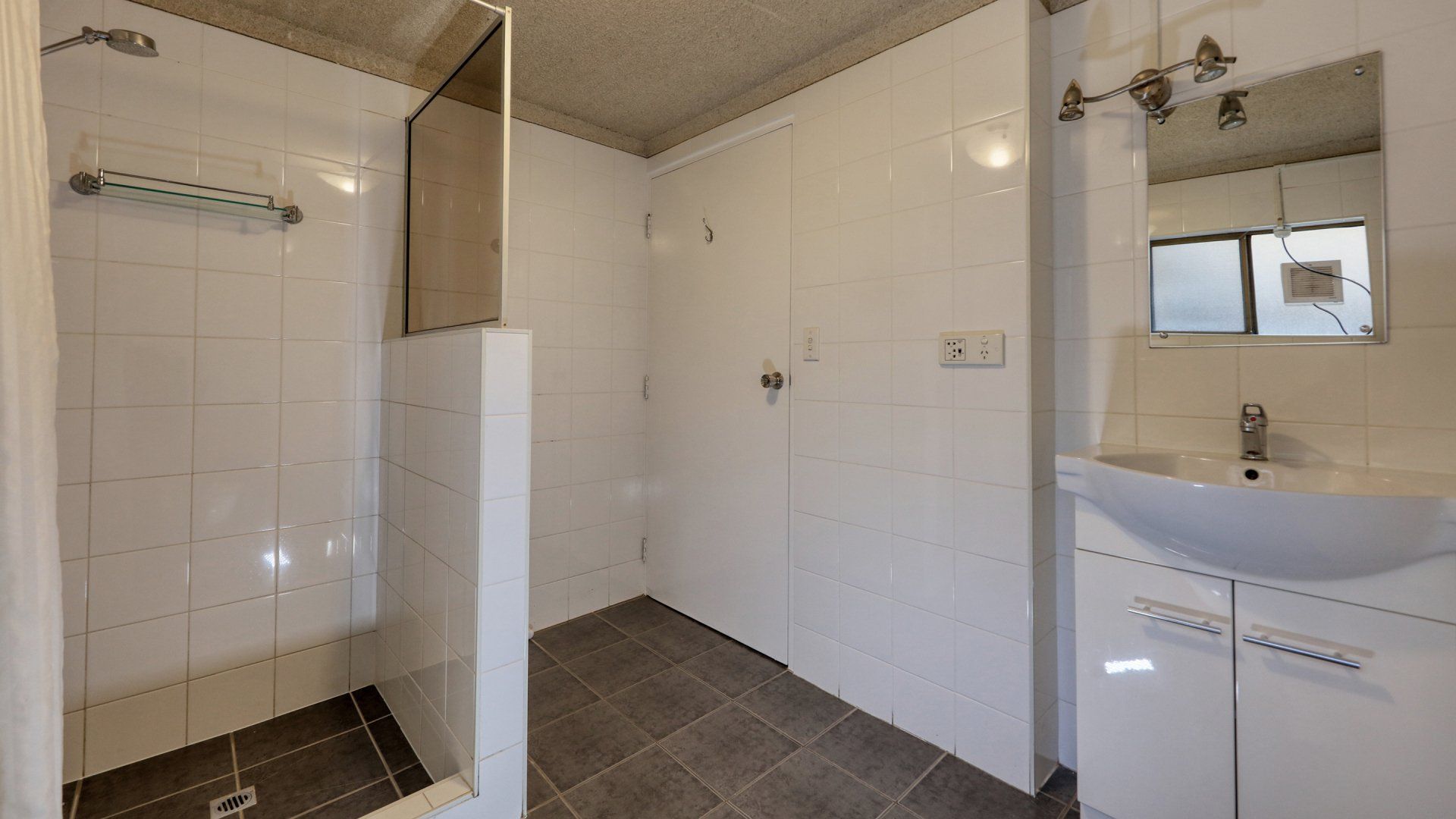 Modern bathroom with tiled shower, white walls, gray floor, sink cabinet, and mirror