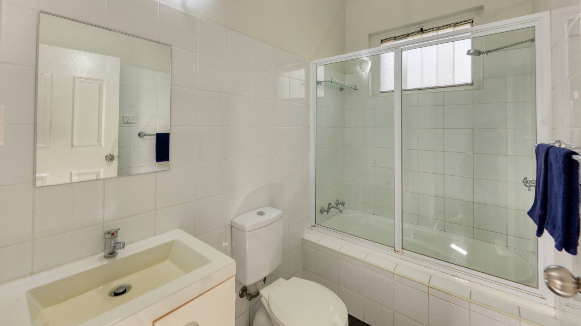 Bright white bathroom with a sink, toilet, bathtub, and glass shower door, seen from the vanity.