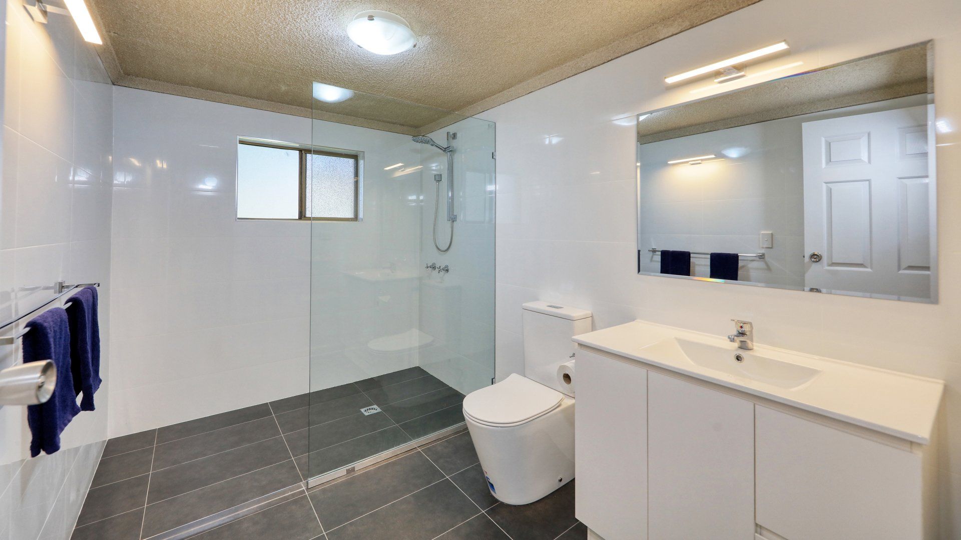 Modern white bathroom with walk-in shower, toilet, vanity, and large mirror