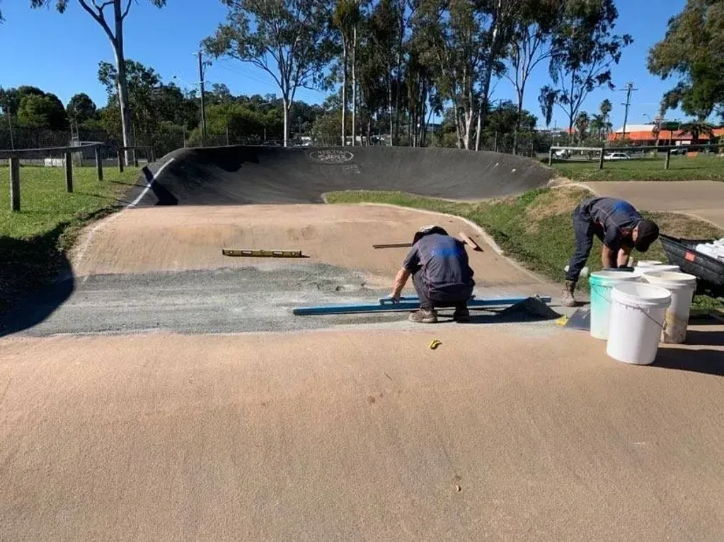 Two men are working on a concrete surface in a park.