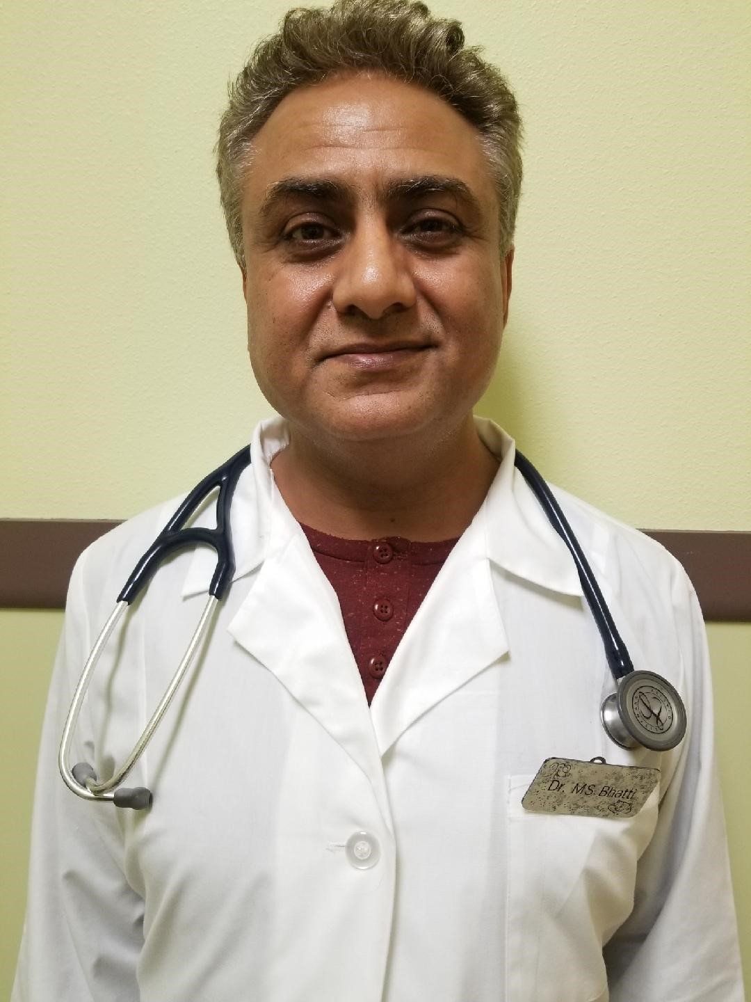 Man in a white lab coat with a stethoscope around his neck, standing indoors.