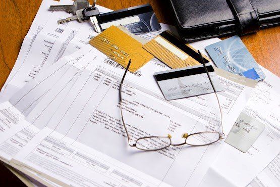 Eyeglass Above the Documents — Seattle, WA — South Seattle Veterinary Hospital Bills, credit cards, keys, glasses, and a wallet on a wooden surface, suggesting financial disarray.