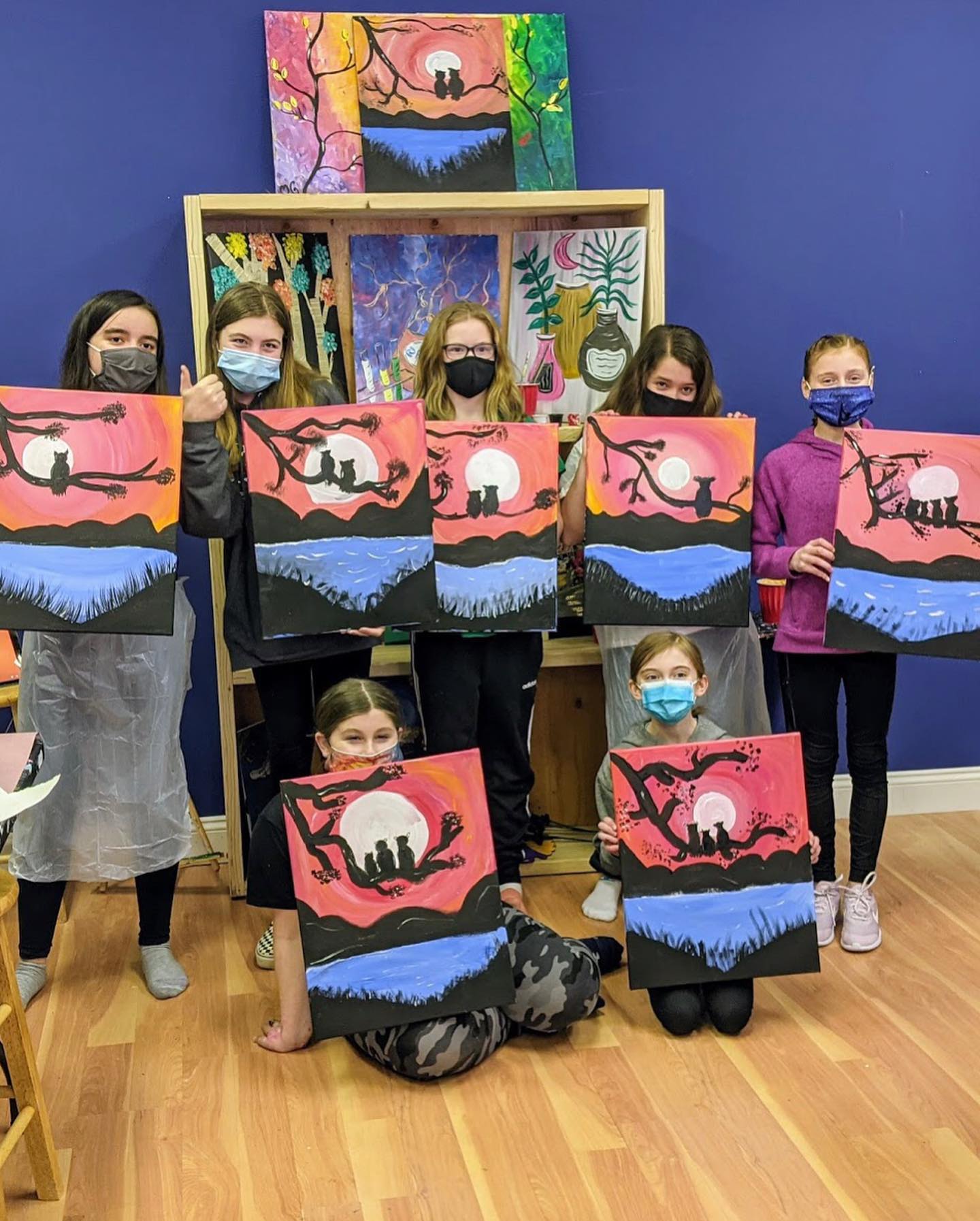 girls posing with canvas paintings from birthday class