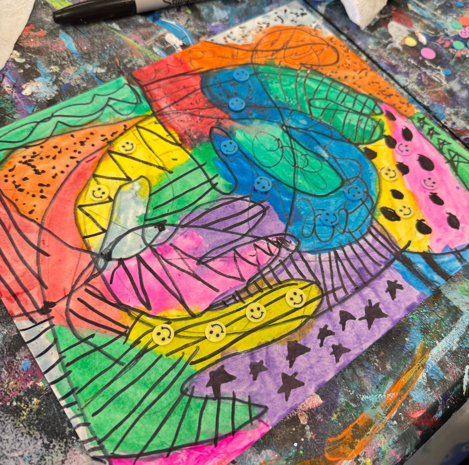Colorful abstract butterfly drawing with rainbow wings and black outlines on a paint-splattered surface