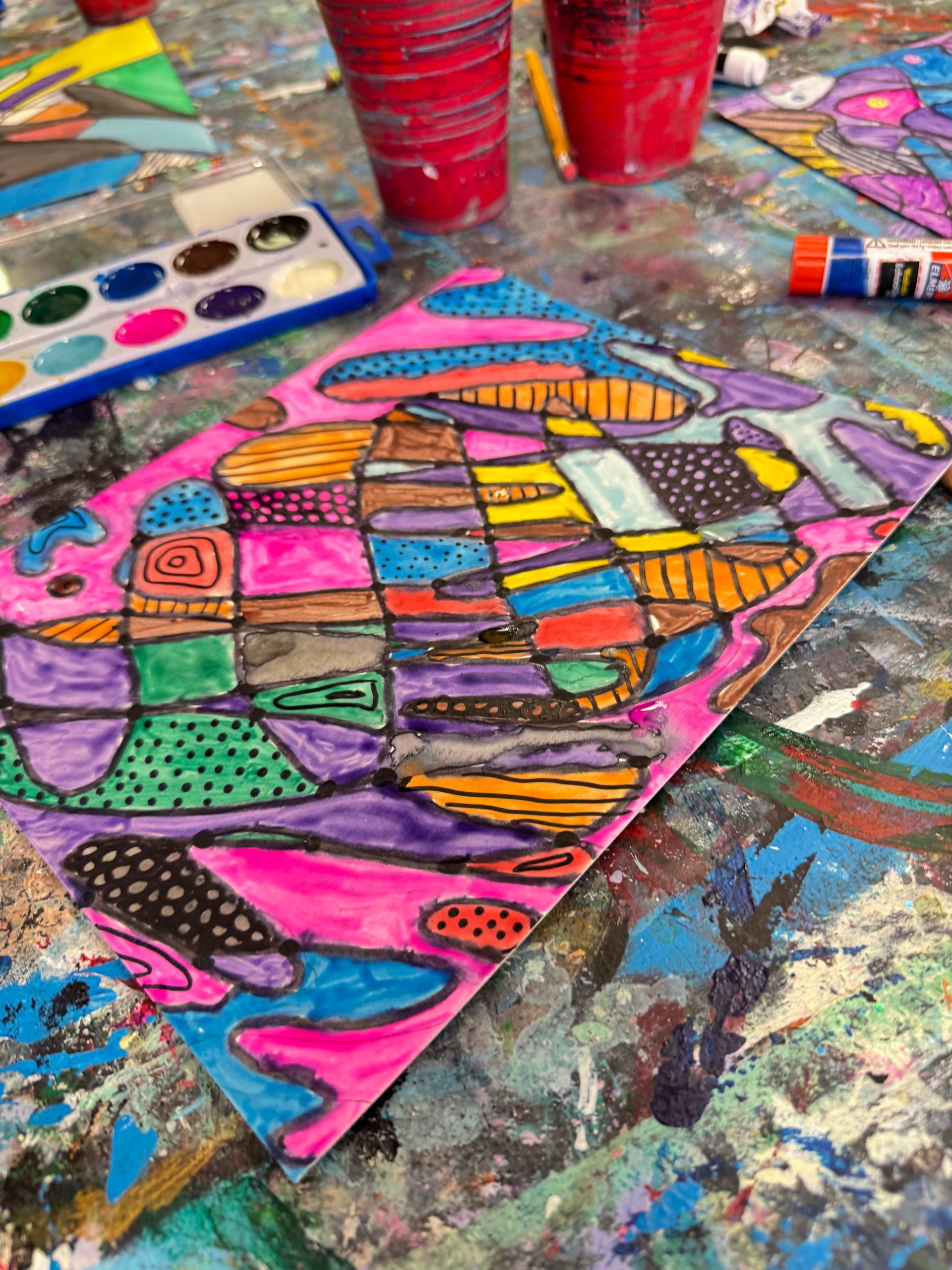 Colorful abstract fish painting on paper, surrounded by art supplies and paint-splattered table