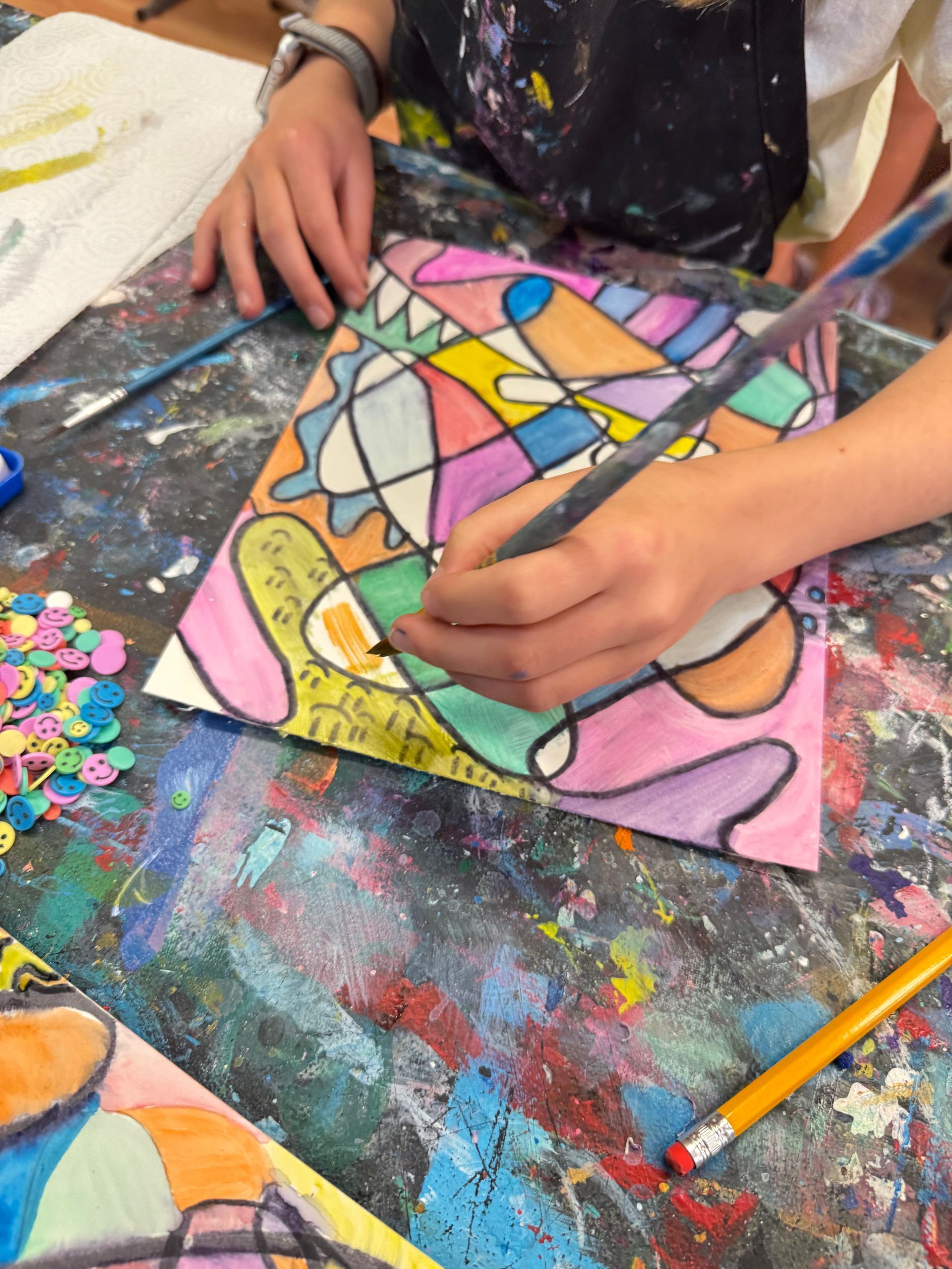 Hands painting a colorful abstract design on canvas at a paint-splattered table