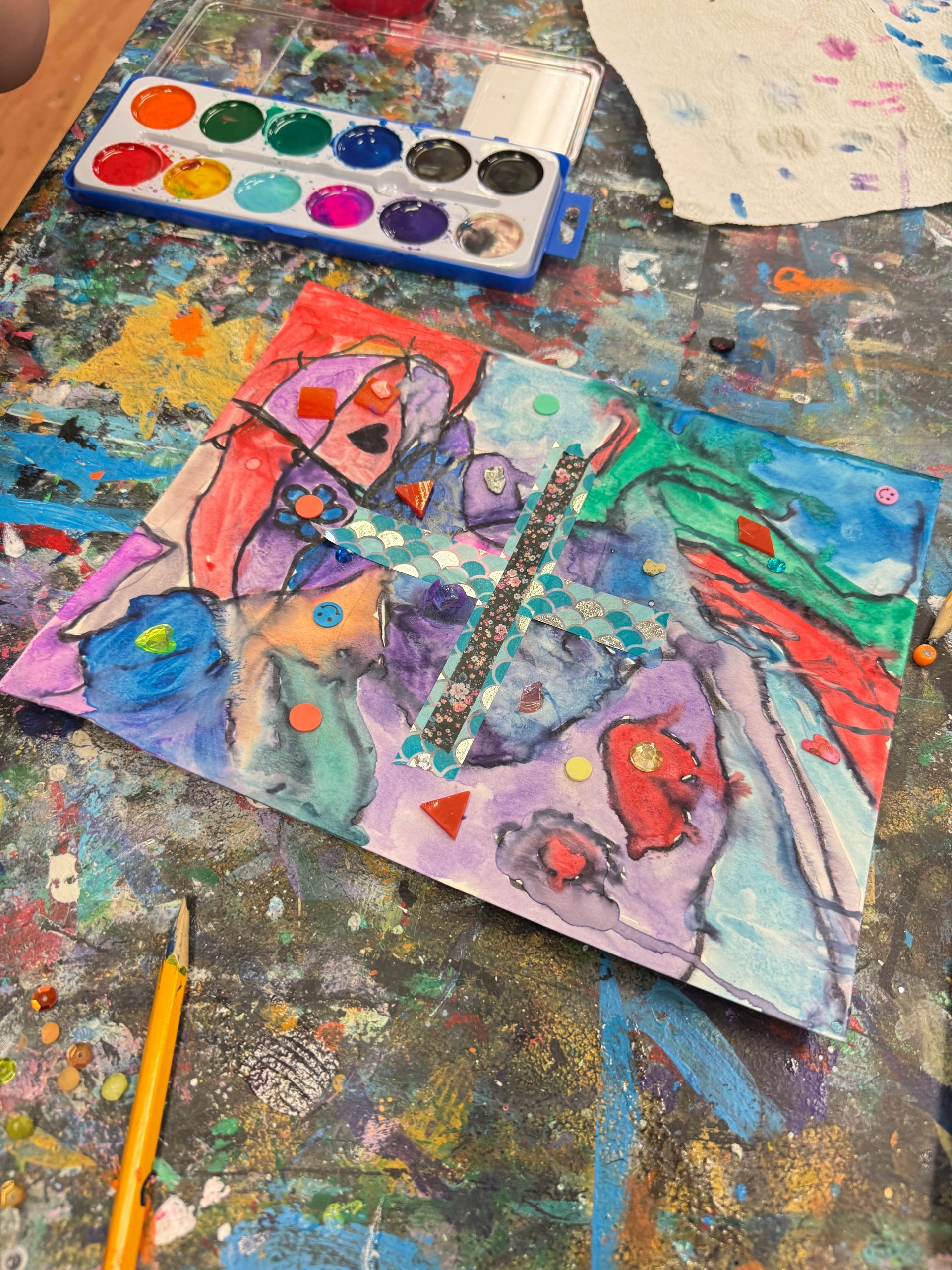 Colorful watercolor butterfly painting on a paint-splattered art table with a brush and pencil nearby