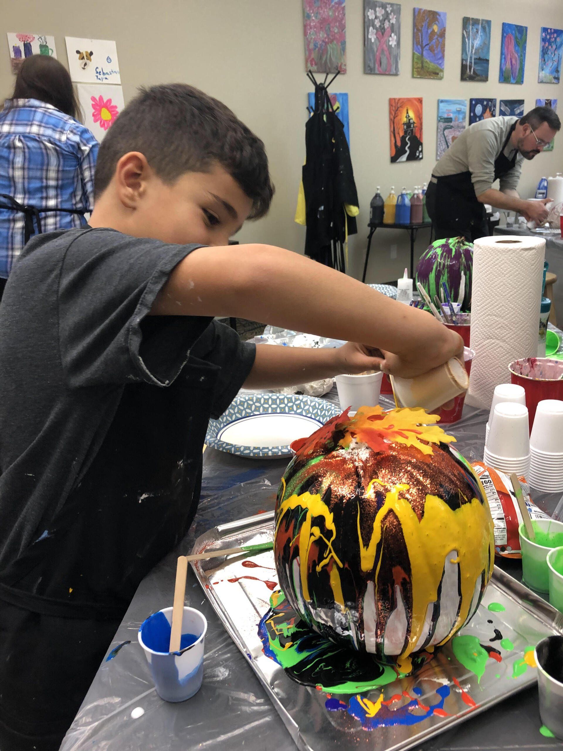 Boy pouring paint over a pumpkin