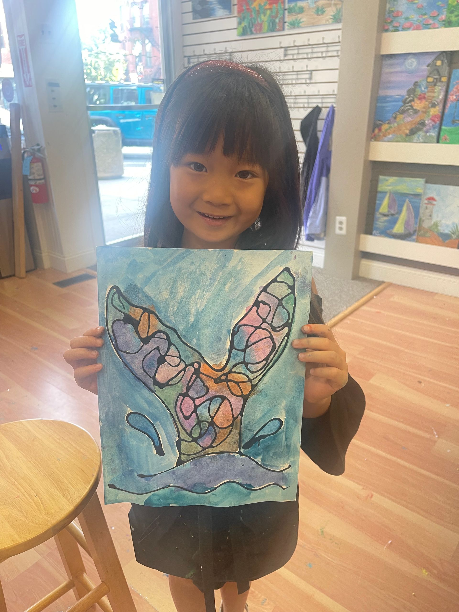 A little girl is holding a painting of a whale 's tail.