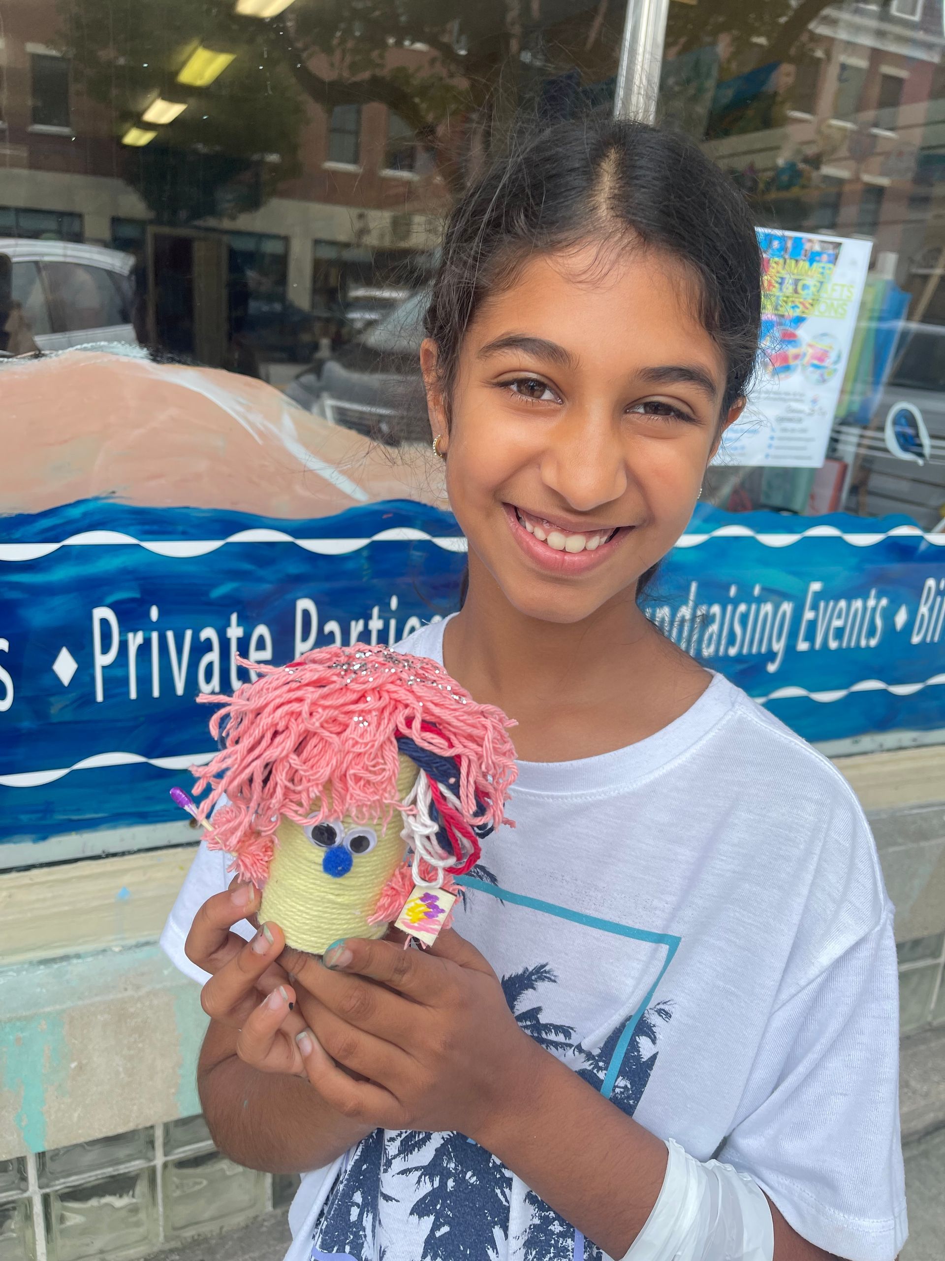 A young girl is holding a stuffed animal in front of a store window.