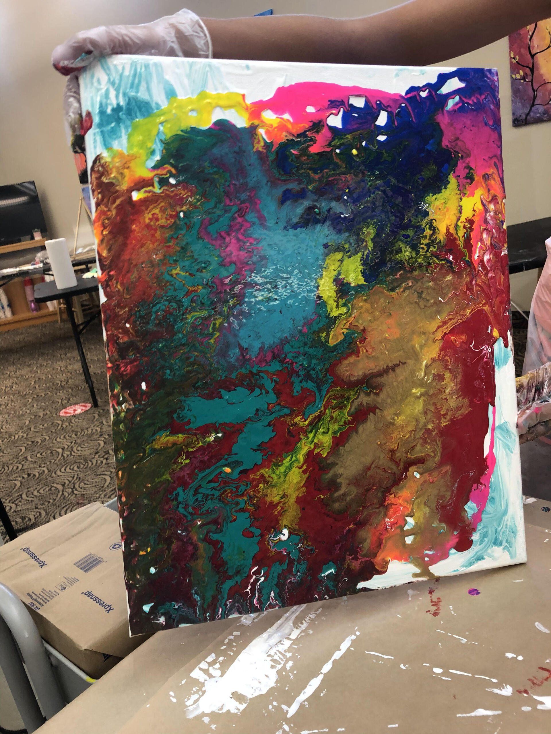 A person is holding a colorful painting on a canvas.