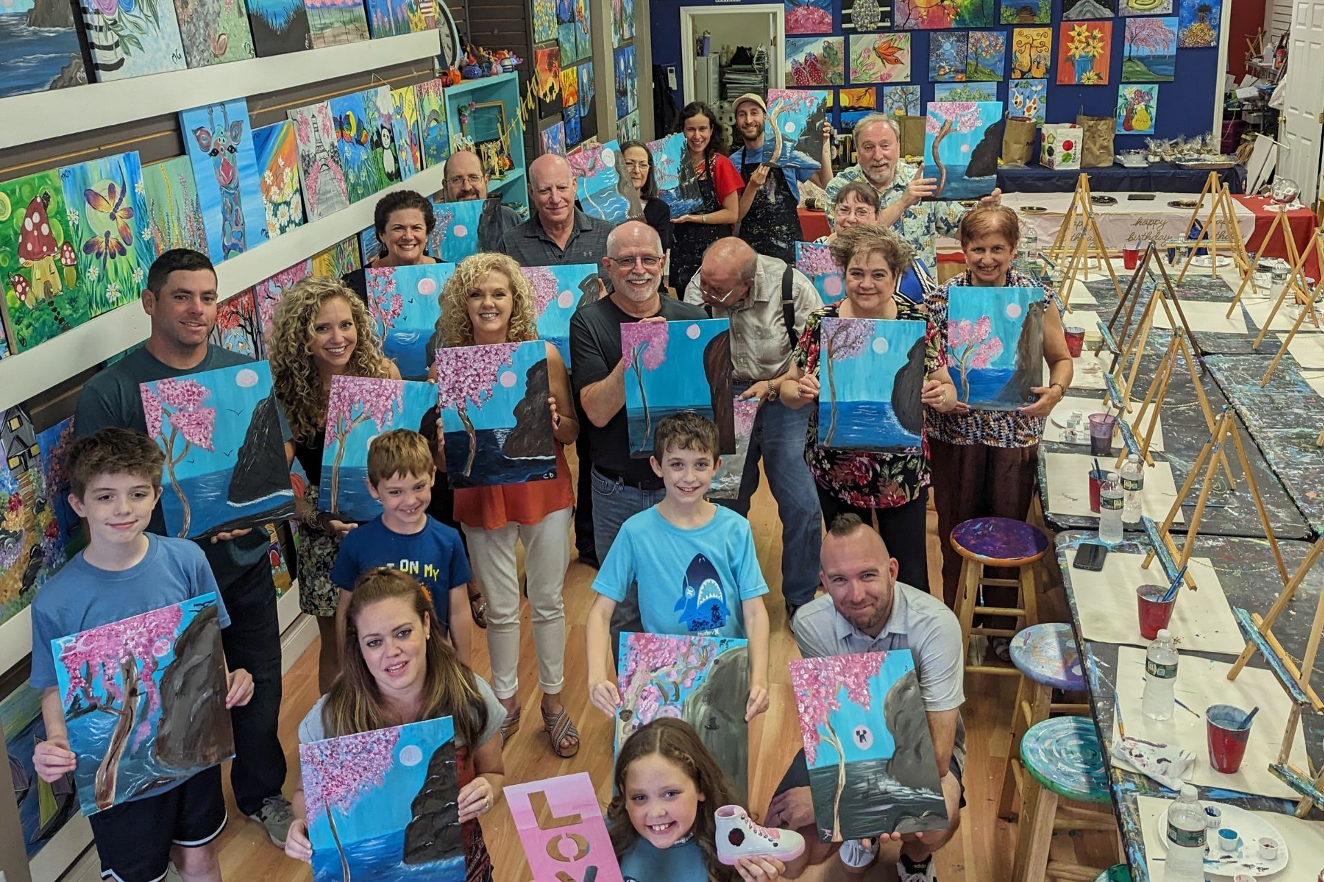 A group of people are standing in a room holding paintings.