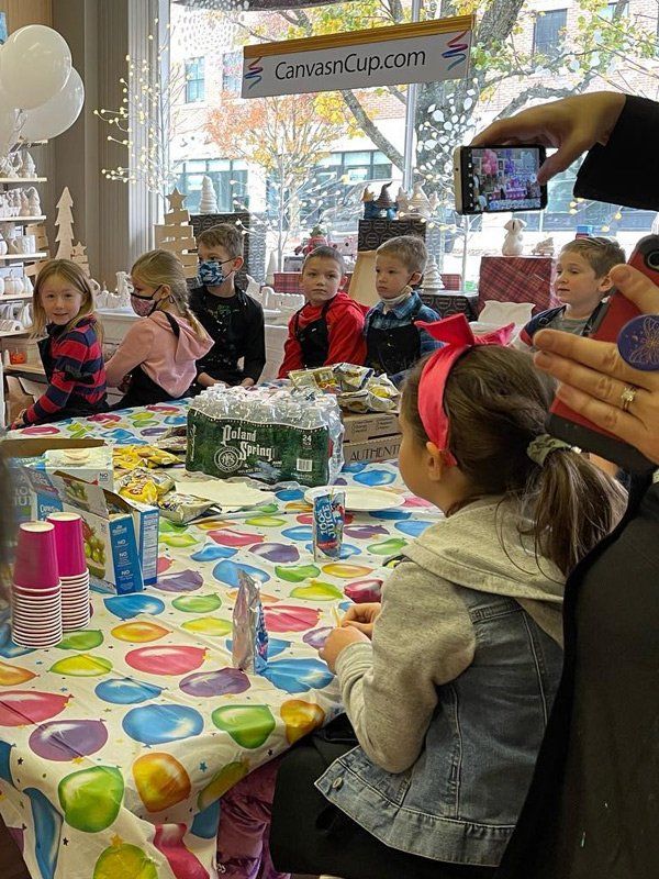 A group of children are sitting at a table with a colorful table cloth.