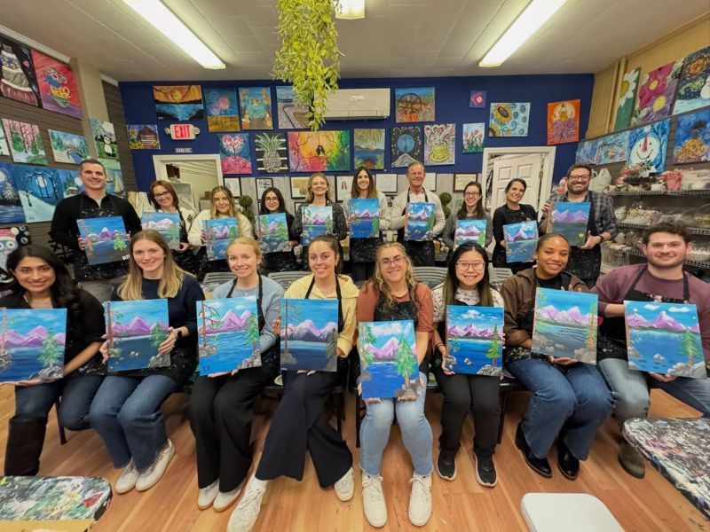 Classroom group holding colorful watercolor artworks, seated and standing in rows.