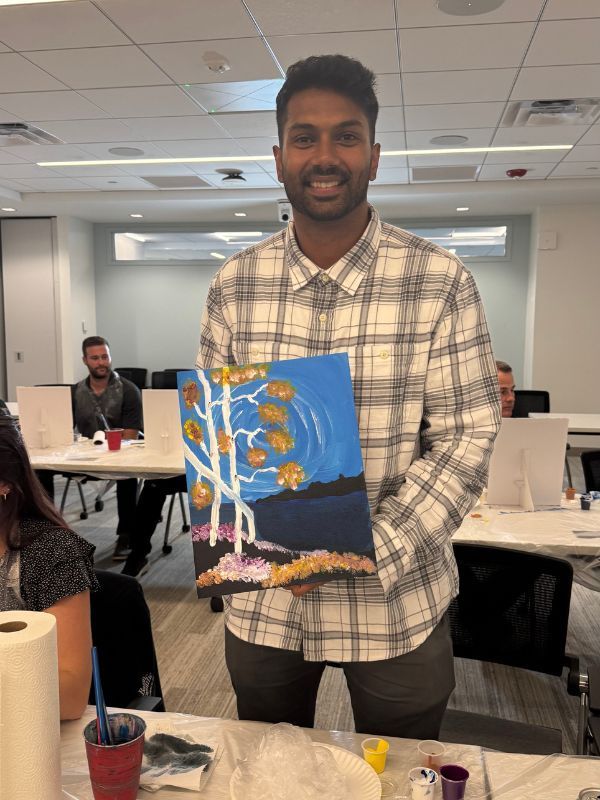  Boston Scientific employee holding a small painted canvas with blue and orange tones in a classroom setting