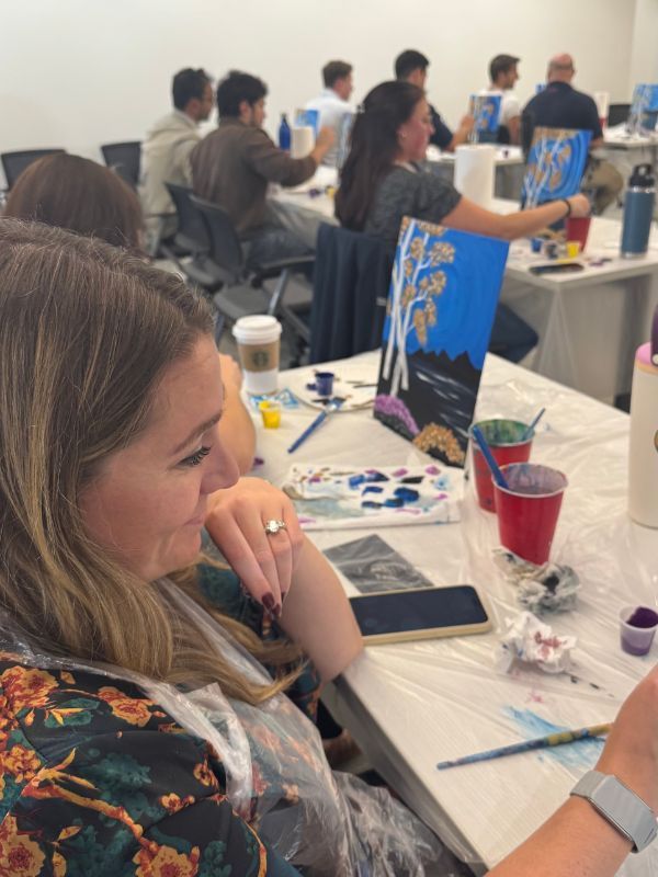  Boston Scientific paint party participants painting at tables, with canvases, brushes, and drinks on a bright white table.