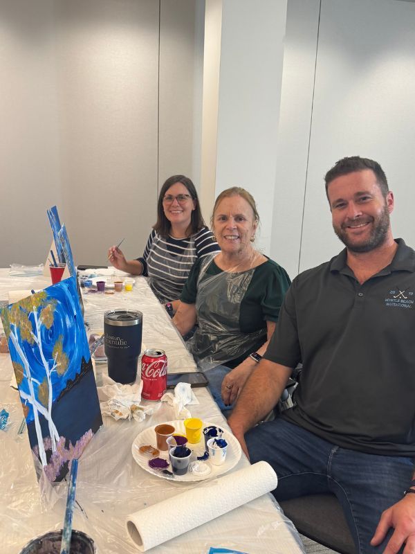 Three people smiling at a team building hybrid paint party.