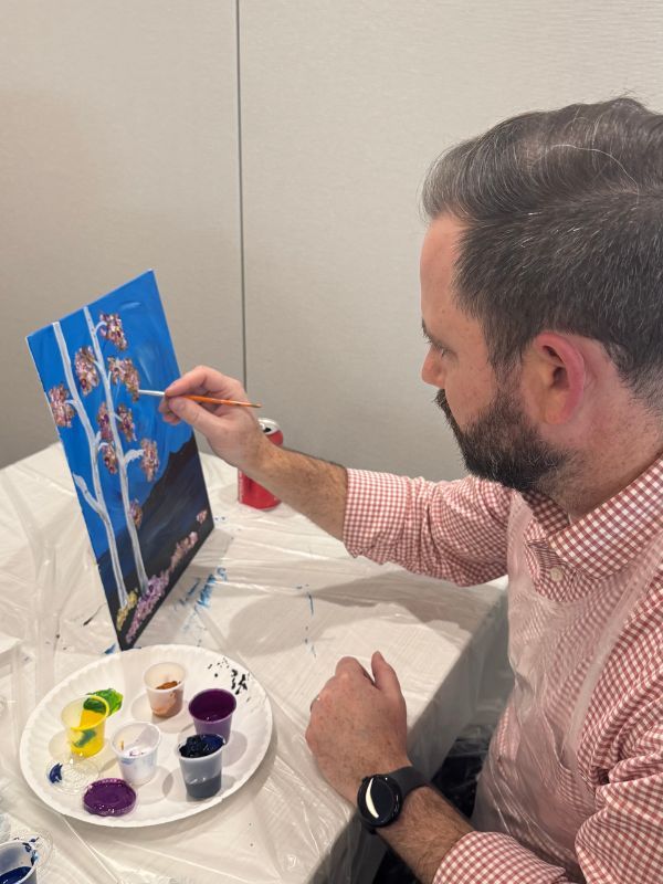  Boston Scientific employee painting a canvas at a table with paint cups and brushes in a craft setting