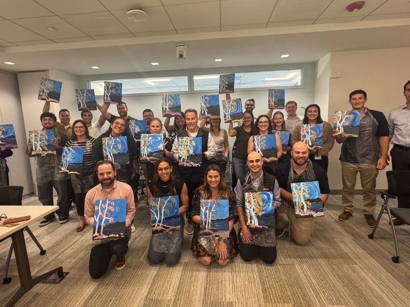  Boston Scientific employees posing indoors, holding painted birch trees canvases