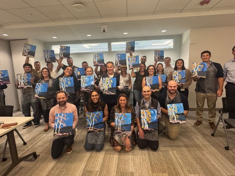 Boston Scientific group of holding painted canvases in a bright room, posing for a team photo.