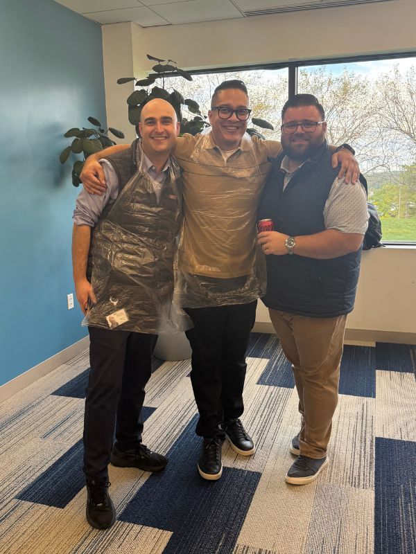  Boston Scientific employees  standing arm-in-arm in an office lobby, smiling in front of large windows at a paint party.
