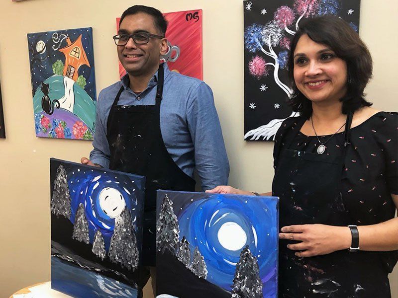 Two smiling artists holding blue abstract paintings in a colorful gallery display