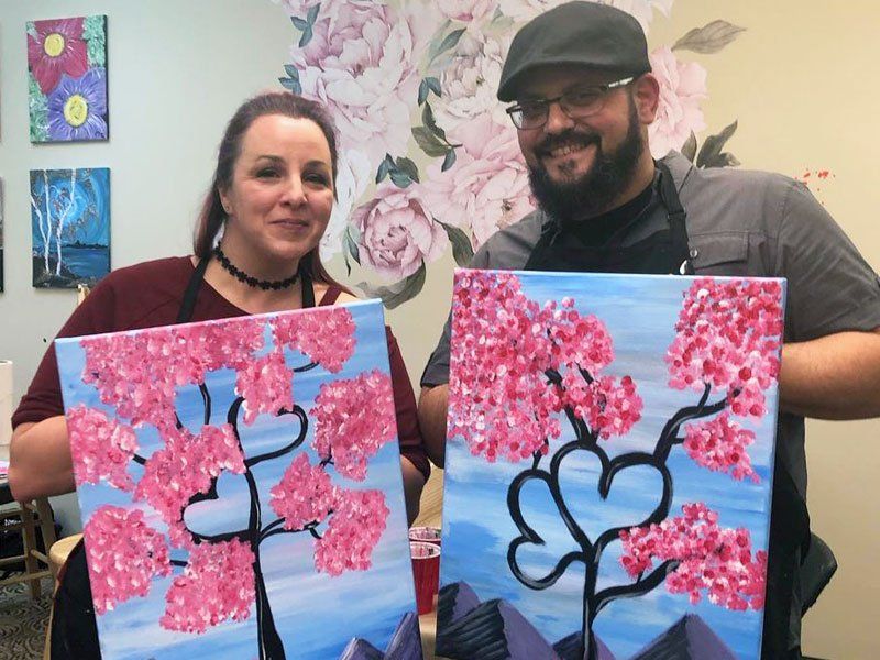 Two people holding blue-and-pink cherry blossom paintings in an art studio