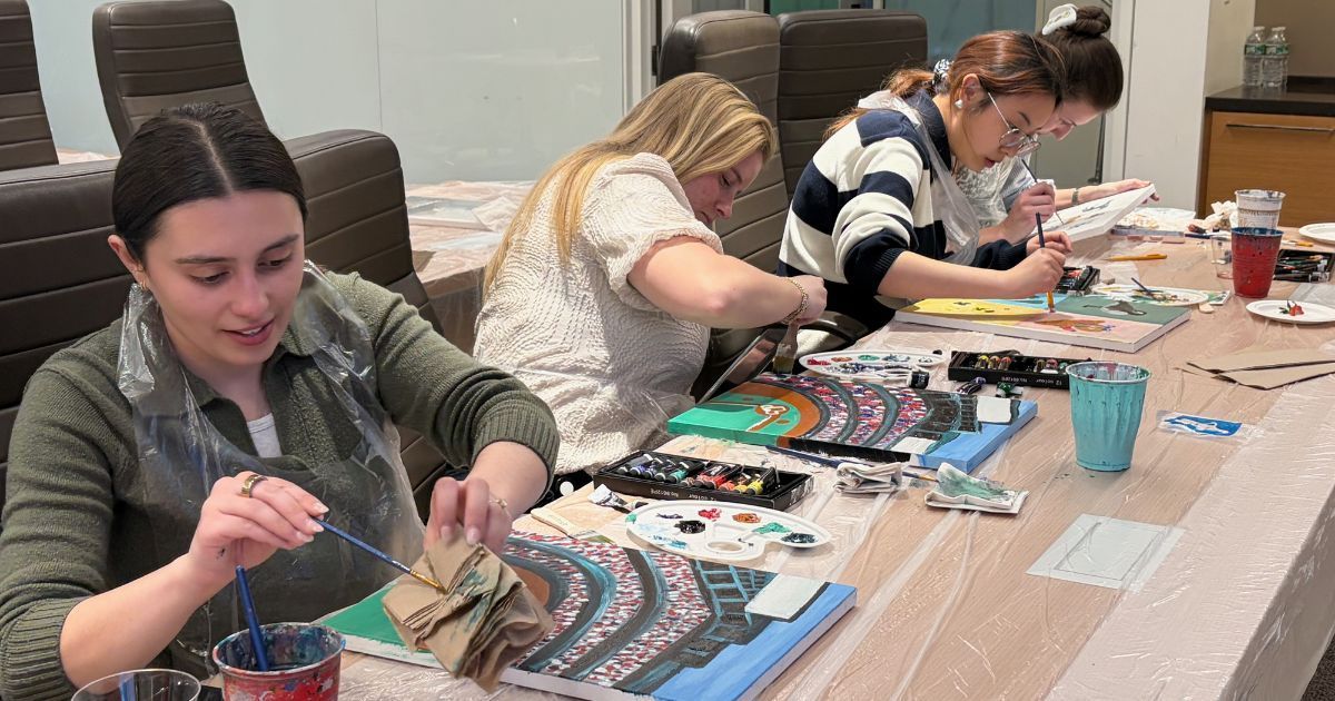 People painting colorful art projects at a table in a bright indoor workshop