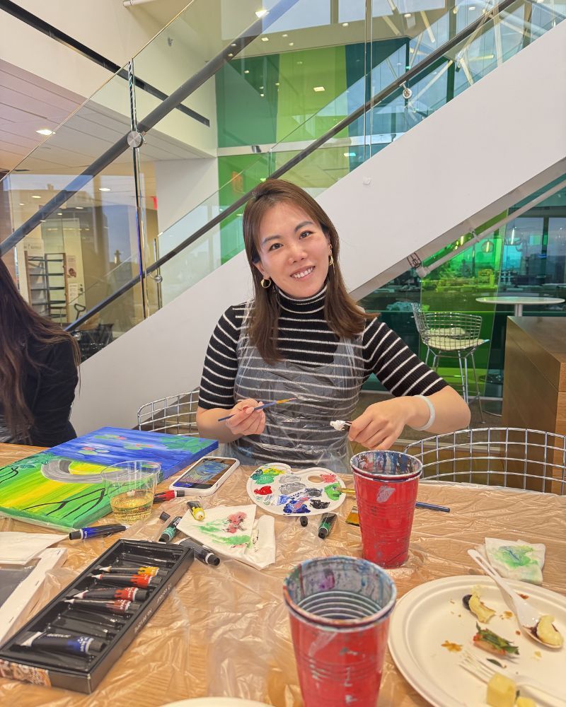 Woman smiling at a craft table with paints and supplies in a bright indoor space