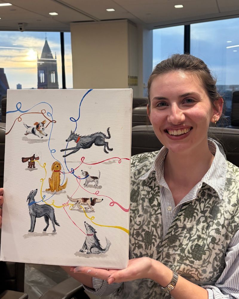 Smiling woman holds a board with colorful hand-drawn animal illustrations in an office with a city view.