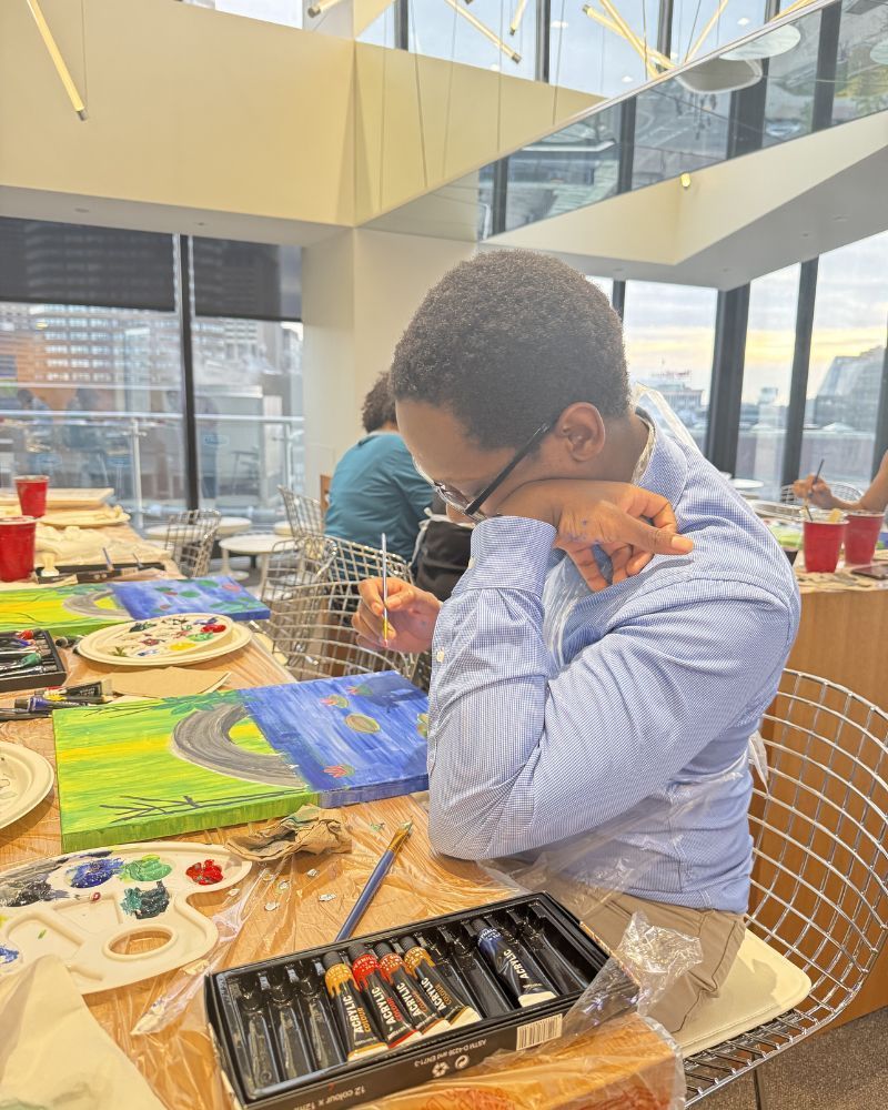 Person painting at a table with brushes and palettes in a bright indoor studio, city view behind them