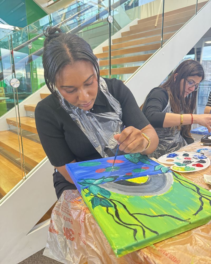 Two people painting colorful canvases at a table in a bright indoor art space