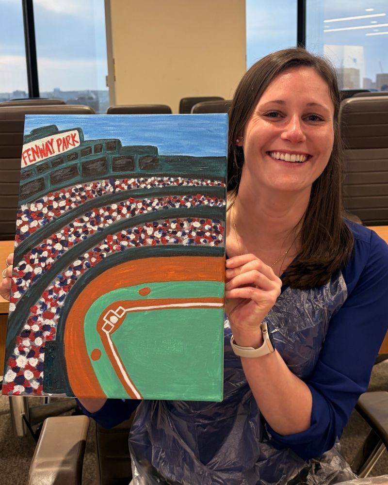 Woman smiling and holding a painting of a baseball stadium in an office setting