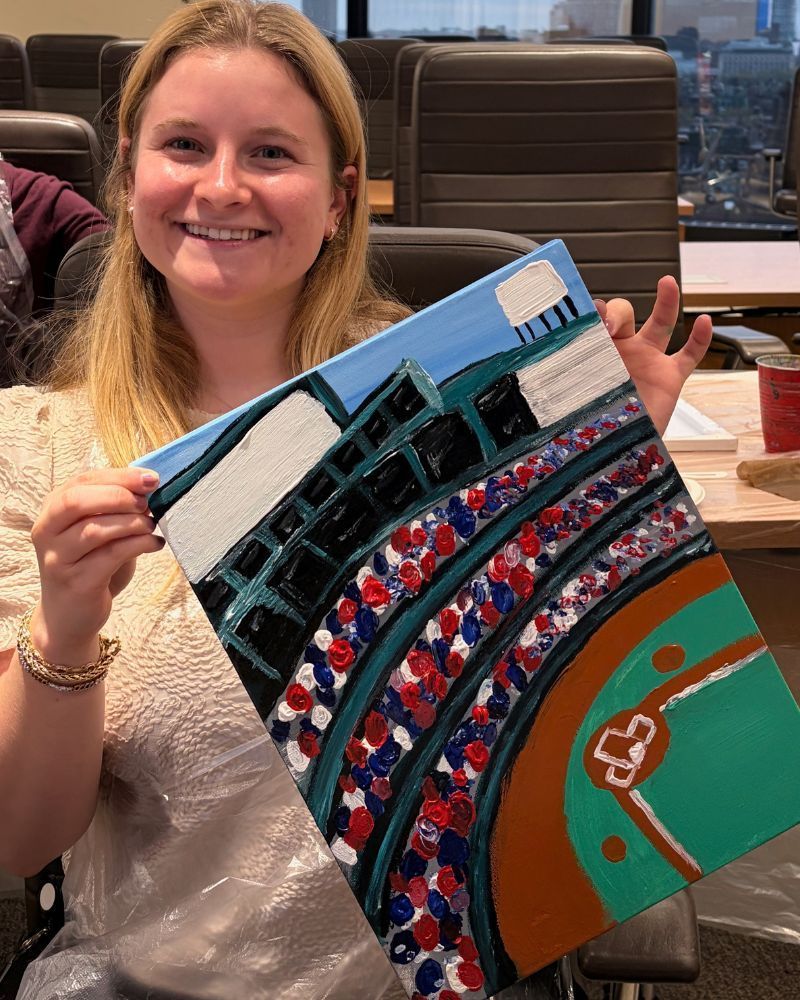 Smiling woman holding a colorful stadium-themed artwork indoors