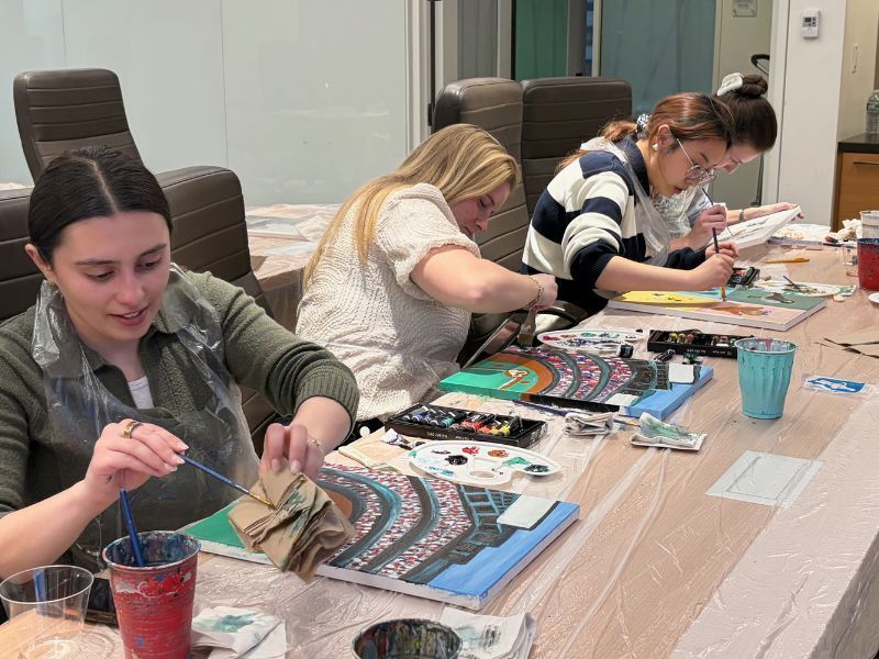 People painting at a long table during a group art activity