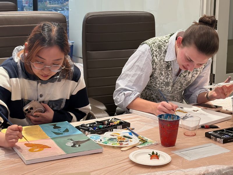 Two people painting at a table with art supplies and red drinks, focused on their work