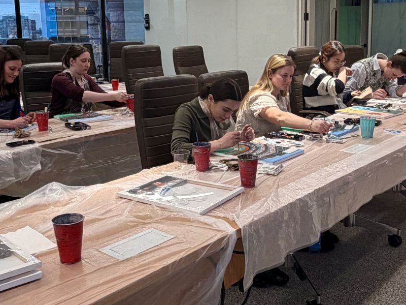 People seated at long tables in a meeting room, writing on papers with cups and notebooks nearby.