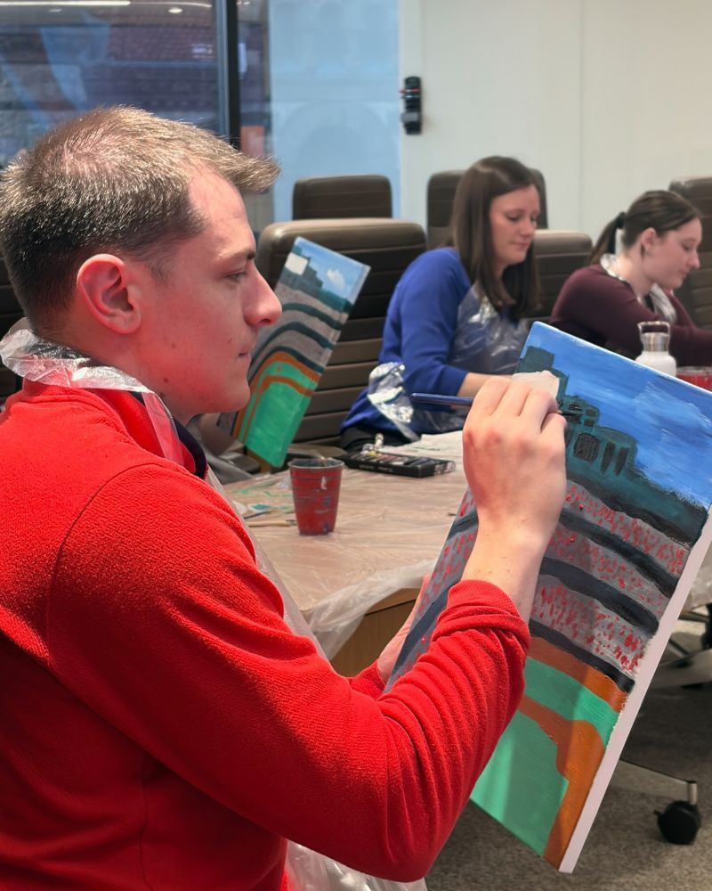 People painting landscapes on canvas at a table in an art class