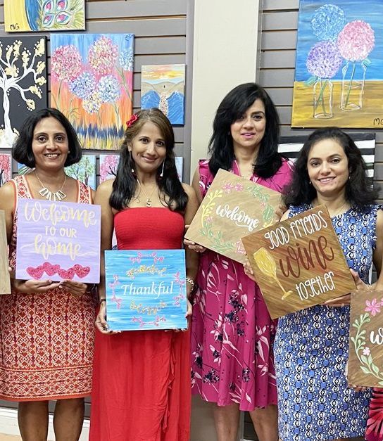 women holding painted wood sign