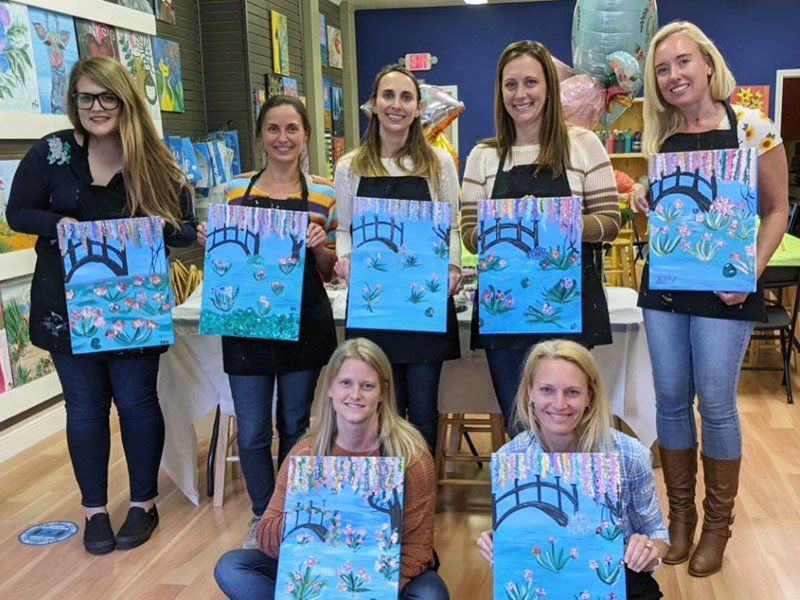 Group at paint and sip party posing with their paintings