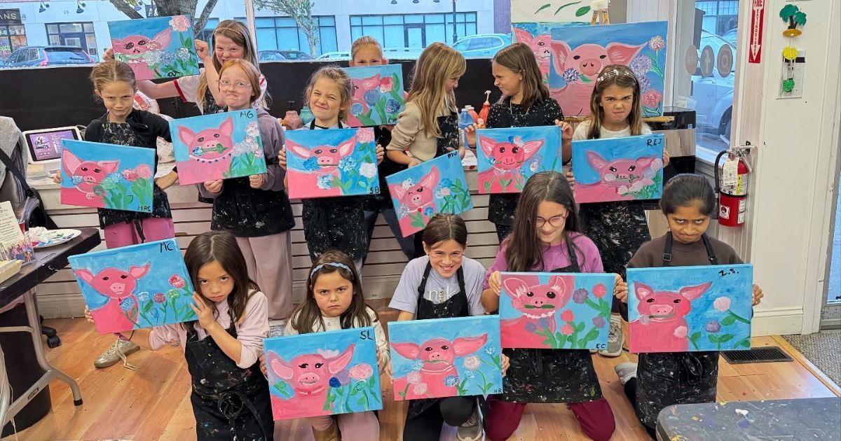Children in a classroom holding bright pink-and-blue cat paintings